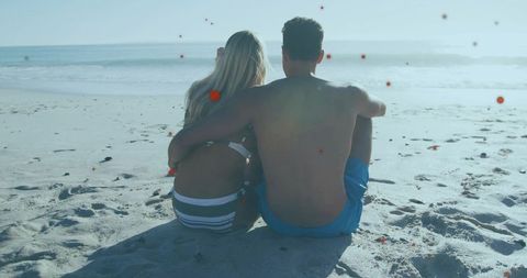 Young couple sitting and embracing on backlit beach watching gentle waves, romantic moment