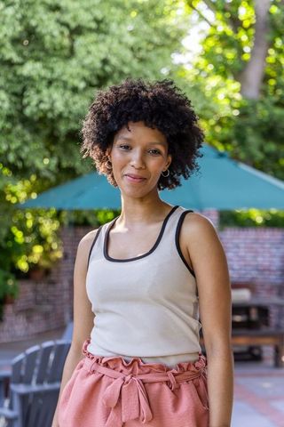 Sunlit african american woman standing in garden courtyard wearing tank and pink shorts