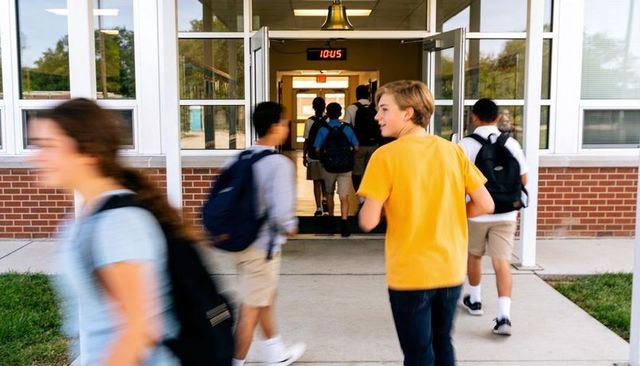 Middle school students walking into entrance turning head toward classmates with backpacks