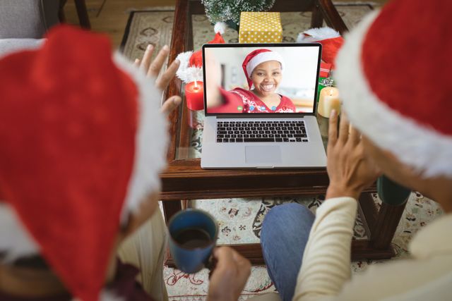 Diverse couple with santa hats having video call with happy african american woman. Christmas, celebration and digital composite image.