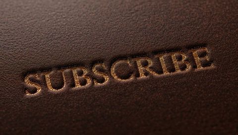 Embossed subscribe gold foil on dark brown leather closeup luxury branding concept