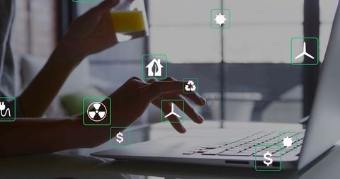 Typing female hands on laptop with sustainability icons, holding juice in home office