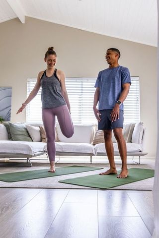 Couple practicing home balance yoga on green mats in bright living room