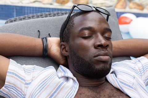 African american man relaxing on poolside lounge chair with sunglasses and striped shirt
