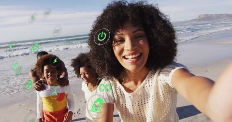 Smiling woman taking selfie with family on sunny beach with augmented reality eco icons