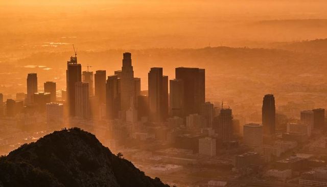 Downtown skyline glowing in golden haze at sunrise from rocky hill with silhouettes