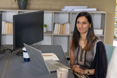 Indian businesswoman working at modern office desk with laptop and coffee mug, minimalist workspace