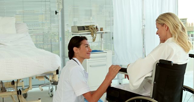 Smiling nurse kneeling and talking with patient sitting in wheelchair in modern, light-filled hospital room. This image can be used to depict caregiving, medical assistance, hospital environment, patient recovery, and healthcare services. Ideal for use in healthcare industry marketing, medical articles, patient care brochures, and rehabilitation services advertising.