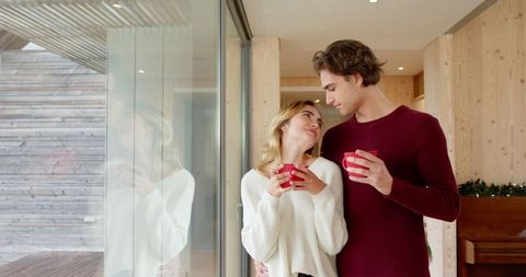 Couple Enjoying Warm Drinks by Glass Door at Home