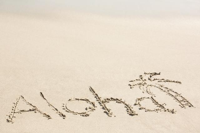 Aloha written in sand on beach, perfect for travel and tourism promotions, summer vacation advertisements, and tropical getaway brochures. Ideal for conveying a sense of relaxation, warmth, and welcoming atmosphere.