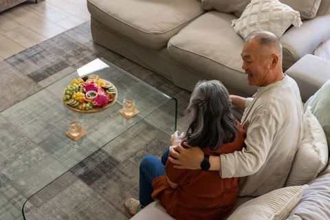 Senior couple enjoying cozy afternoon on sofa sharing fruit platter on glass coffee table