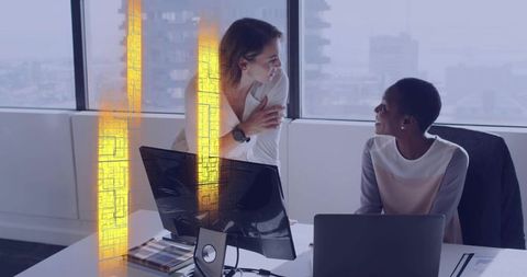 Female colleagues discussing project in modern office with city skyline and laptops