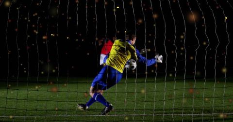 Diving goalkeeper making dramatic nighttime save through goal net under floodlights