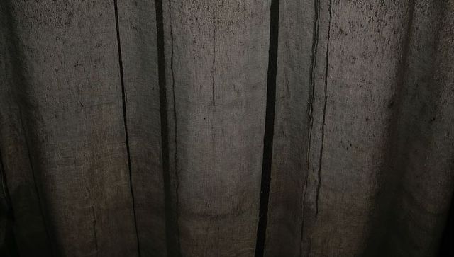 Dark linen curtain closeup showing vertical seams, pleats and woven texture with backlight