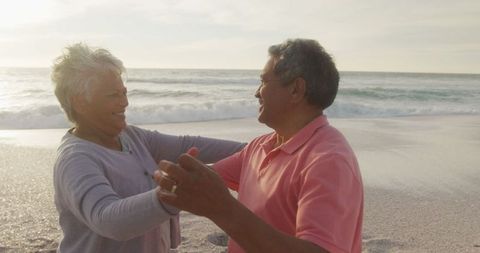 Happy Senior Couple Dancing Joyfully on Beach at Sunset