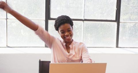 Joyful woman celebrating success with laptop at work