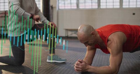 Fitness coach monitoring wearable data while athlete holds forearm plank in gym studio