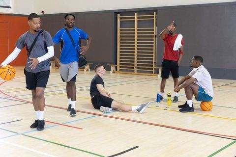 Male teammates warming up, resting and chatting on indoor basketball court during pickup game