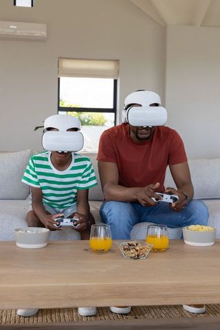 Black father and son gaming with vr controllers on couch