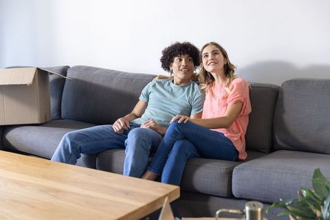 Young couple relaxing on gray sofa in new home beside moving box, sharing affectionate moment