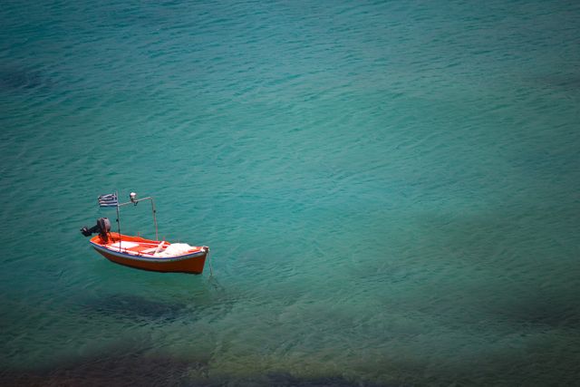 Red boat floating alone on calm turquoise sea, creating a tranquil and serene scene. Great for travel, vacation, or nature websites, as well as for promoting relaxation or exploring the beauty of maritime landscapes.