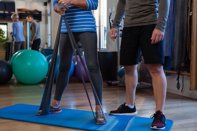 Physiotherapist assisting patient in performing resistance band exercise in a clinic. Useful for illustrating physical therapy, rehabilitation, fitness training, and healthcare support. Ideal for health and wellness blogs, medical websites, and fitness guides.