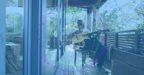 Senior man playing acoustic guitar on sunny porch with digital wireframe globe overlay