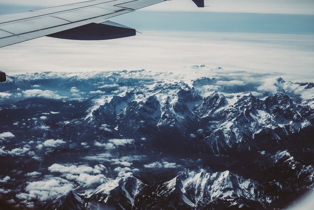 A breathtaking snapshot capturing an expansive view of snow-covered mountains. The scene highlights the airplane wing, emphasizing the essence of air travel. Ideal for travel agencies promoting adventure trips, flight companies advertising flight experiences, or nature documentaries illustrating majestic aerial sceneries. Could be used in travel blogs or websites emphasizing wanderlust and exploration.