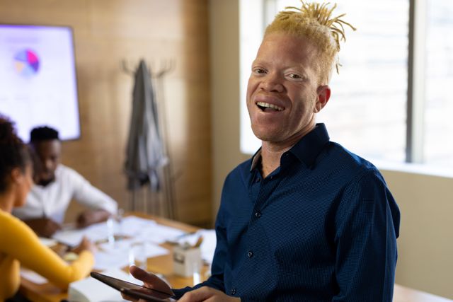 Portrait of smiling african american mid adult albino businessman with colleagues in background. unaltered, abnormal, technology, corporate business, occupation and office concept.