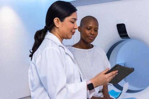 Female clinician reviewing tablet with patient beside mri scanner radiology consultation