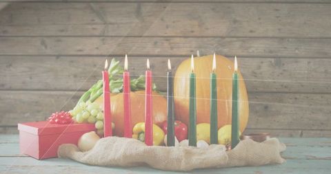 Kwanzaa kinara glowing with seven lit candles amid harvest still life of pumpkin and grapes