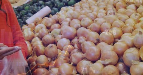 Shopper selecting fresh onions from market display while holding bag and mobile device