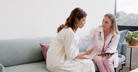 Female doctor consulting with patient on sofa using tablet showing compassionate care