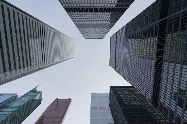 Tall skyscrapers in a financial district viewed from below, emphasizing modern architecture and urban landscape. Ideal for use in business publications, articles on urban development, real estate promotions, and finance-related content.