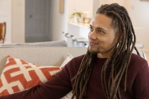 African american man with dreadlocks smiling on modern living room sofa