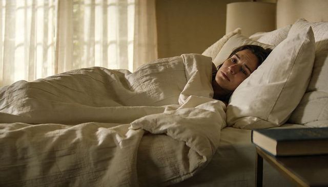 Woman lying awake under neutral duvet, contemplating in soft morning light, cozy bedroom