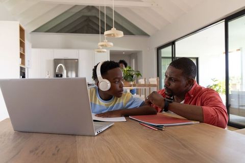 African american father helping teen son with homework at modern kitchen table