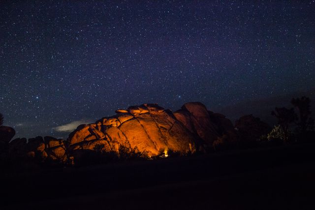 Captivating night scene showing campfire surrounded by large rocks under a starry sky. Ideal for use in travel blogs, camping and adventure itinerary sites, nature magazines, and inspirational posters.