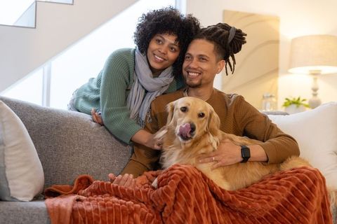 African american couple cuddling golden retriever on cozy living room sofa