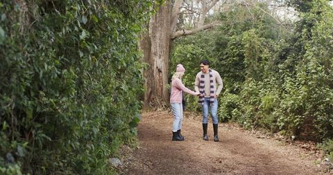 Couple holding hands and walking on winter woodland trail wearing knit hat and scarf