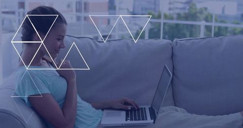 Young woman working remotely on laptop while reclining on sofa with geometric overlay