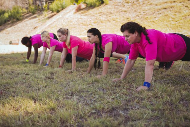Group of women participating in an outdoor boot camp, performing push-ups on grass. Ideal for promoting fitness programs, outdoor activities, group exercise classes, and health and wellness campaigns.