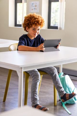 African american schoolboy using tablet at classroom desk, focused learning in daylight