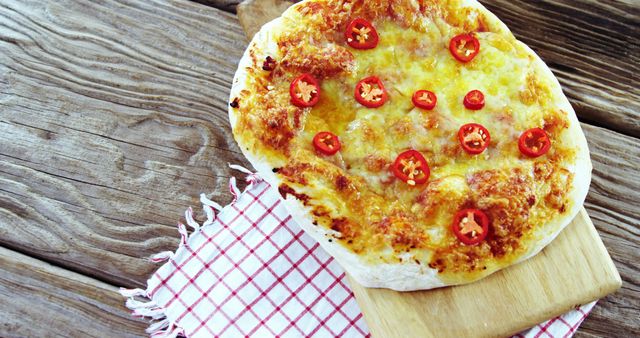 A freshly baked cheese pizza topped with spicy red chili peppers rests on a wooden board, with copy space. Its tempting appearance makes it ideal for culinary themes and discussions about spicy food variations.