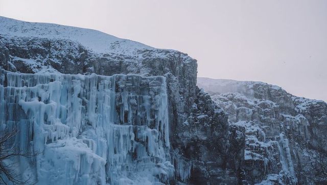 Frozen waterfall cascading into giant icicles on snow-covered cliff in arctic twilight