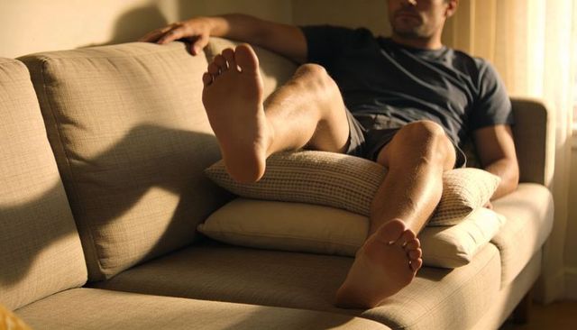 Man relaxing on beige sofa with bare feet up, cushions and warm natural light
