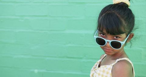 Stylish child posing with sunglasses against green wall