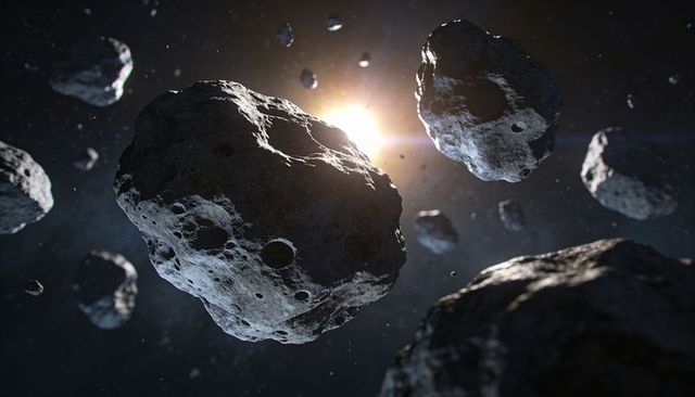 Rimlit cratered asteroid drifting through debris field with sun backlight and deep space