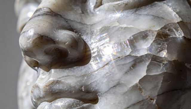 Macro close-up of carved marble face revealing translucent nose, iridescent mineral veins