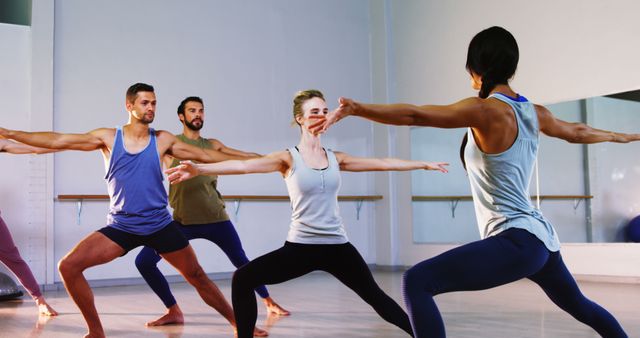 Group of diverse individuals practicing yoga in studio, performing Warrior Pose with focus and balance. Ideal for content related to health, fitness, yoga classes, wellness retreats, and promoting physical activity. Use in marketing for gyms or yoga studios.
